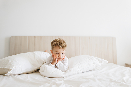 adorable toddler boy in white bodysuit lying on bed at home
