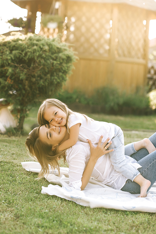 happy mother and little daughter hugging each other while resting on cloth together on backyard