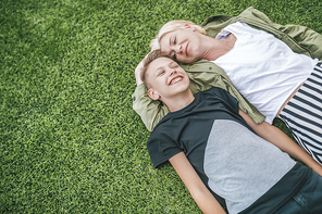 high angle view of happy mother and son laughing while lying together on green grass