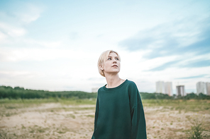 beautiful pensive blonde woman looking up at cloudy sky