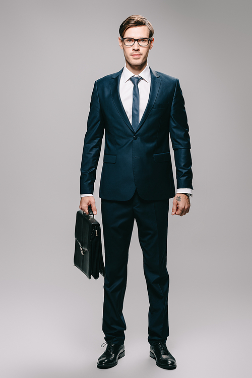 confident businessman in suit holding briefcase on grey background