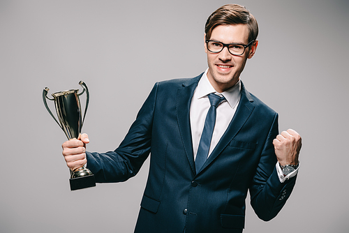 handsome businessman in glasses celebrating victory and holding trophy in hand on grey background