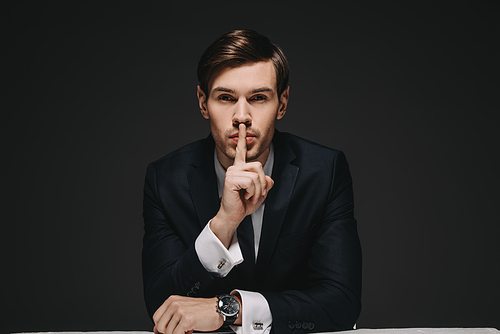 handsome man in suit showing hush sign isolated on black