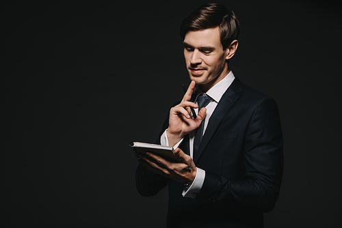 smiling businessman looking at notebook isolated on black