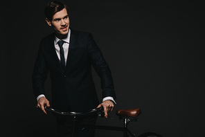 cheerful  businessman in suit holding bicycle isolated on black
