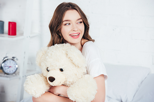 selective focus of smiling woman smiling and hugging teddy bear in bed