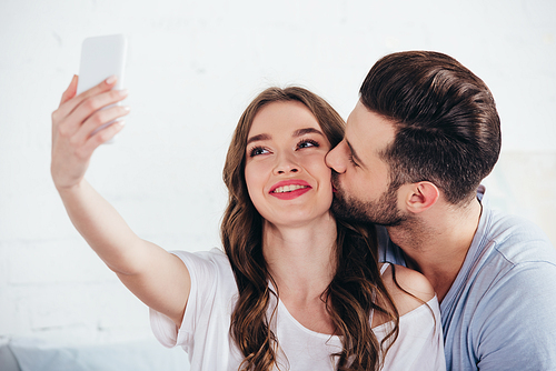 boyfriend kissing girlfriend while taking selfie in bedroom