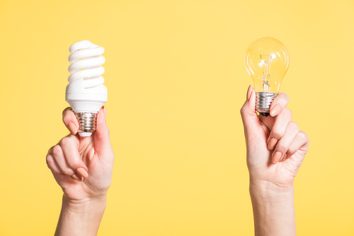 cropped view of woman holding fluorescent and led lamps in hands isolated on yellow, energy efficiency concept
