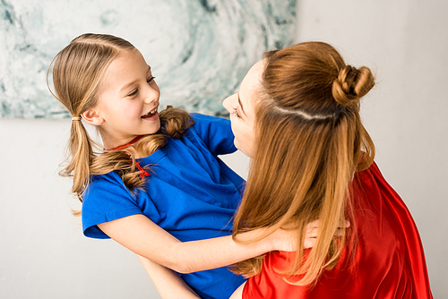 Smiling mother and kid in red cloaks looking at each other