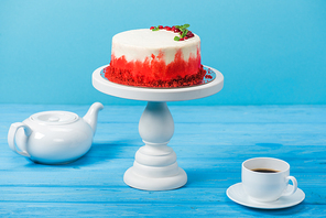 cake decorated with red currants and mint leaves, white cup and tea pot isolated on blue