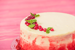 close up of white cake decorated with red currants and mint leaves