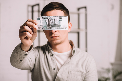 young man hiding face behind russian rubles banknote