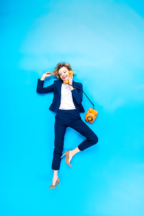 Elegant woman in suit and high-heeled shoes talking on telephone on blue background