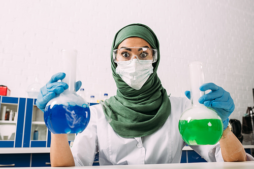 surprised female muslim scientist  and holding flasks during experiment in chemical laboratory