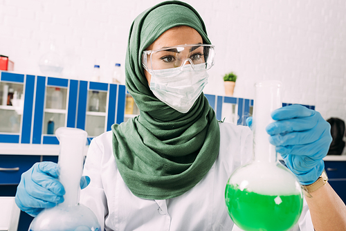female muslim scientist holding flasks during experiment in chemical laboratory