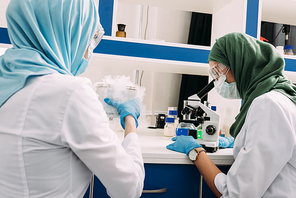 female muslim scientists experimenting with dry ice and using microscope in chemical laboratory