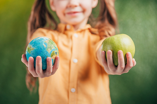 selective focus of child holding globe model and apple on blurred background, earth day concept