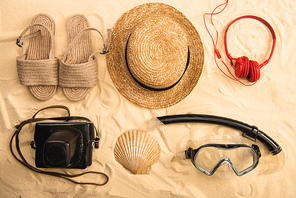 top view of summer accessories, swimming mask with snorkel, headphones and film camera on sand