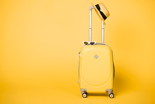 bright yellow suitcase, sunglasses and straw hat on yellow background