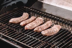 raw pork sausages cooking on barbecue grill grates