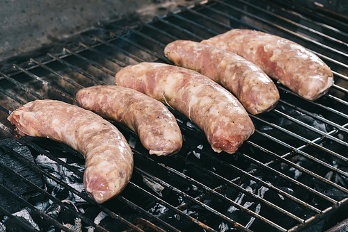 raw fresh sausages cooking on barbecue grill grate