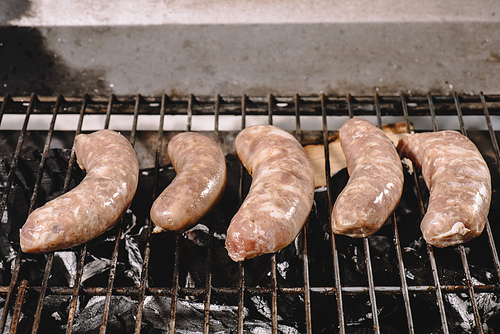 raw fresh sausages cooking on barbecue grill grate with burning coals