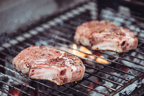 selective focus of juicy raw steaks grilling on barbecue grid with smoke