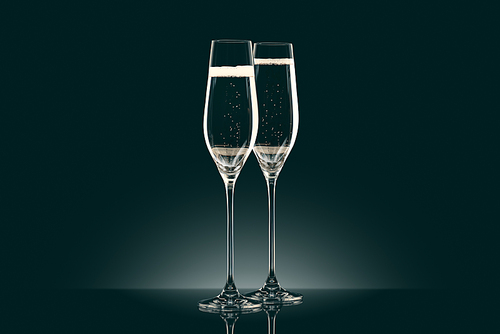 two transparent glasses of champagne on black