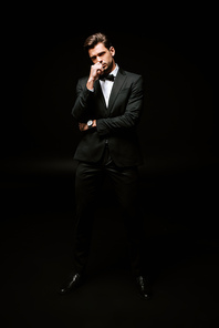 handsome man standing and touching face on black