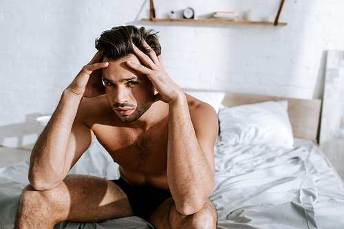 shirtless man  while sitting on bed and touching head