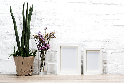 close up view of empty photo frames and flowers on wooden table