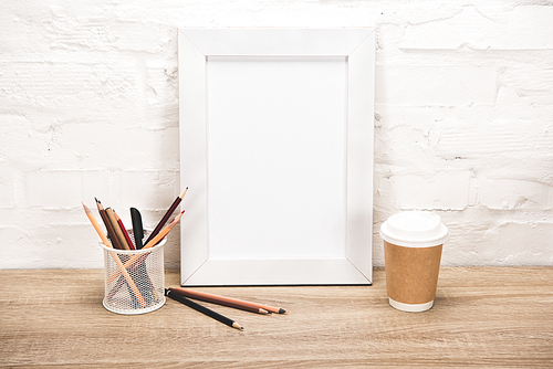 empty photo frame, office supplies and coffee to go on wooden table