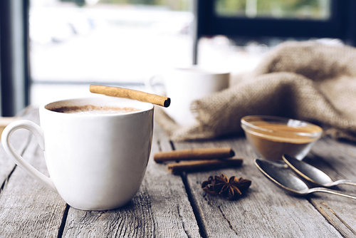 close up view of cup of aromatic cacao with cinnamon stick on wooden table