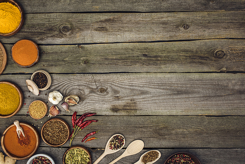 Top view of different spices in bowls and spoons on a wooden tabletop