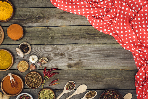 Top view of red tablecloth and different spices on a wooden table