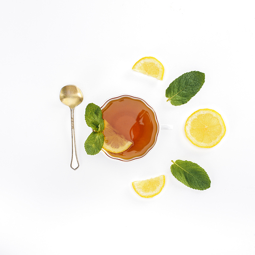 top view of tea in glass, spoon, lemon slices and peppermint on grey