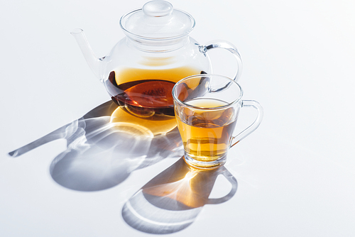 close-up view of healthy herbal tea in glass cup and kettle with shadows on grey