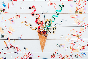 top view of confetti spilling out waffle cone on white wooden table