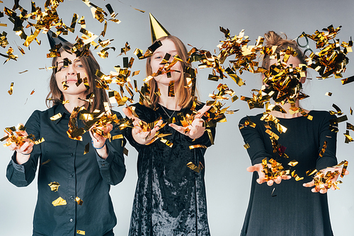 group of attractive young women throwing up golden confetti, isolated on grey