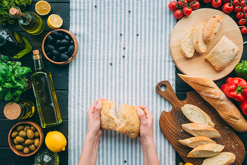 Top view of cropped hands holding bread on table with vegetables and towel