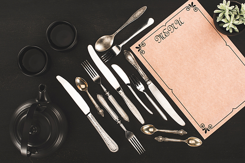 top view of decorative blank menu, vintage cutlery and tea set on black