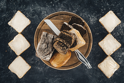 top view of toasts with butter and multigrain bread with knife on wooden cutting board