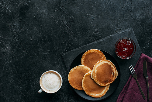 top view of freshly baked pancakes with jam and coffee on black surface