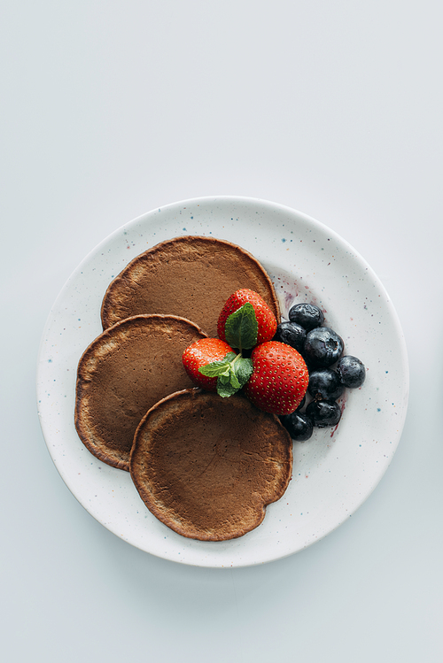 top view of chocolate pancakes with berries on white table