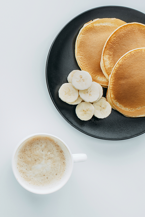 top view of pancakes with sliced banana and cup of coffee on white table