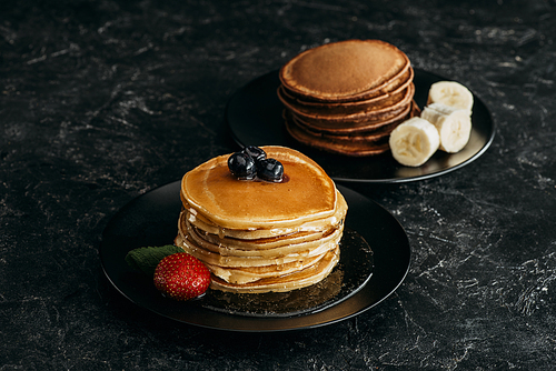plates with stacks of tasty pancakes with fruits on black table