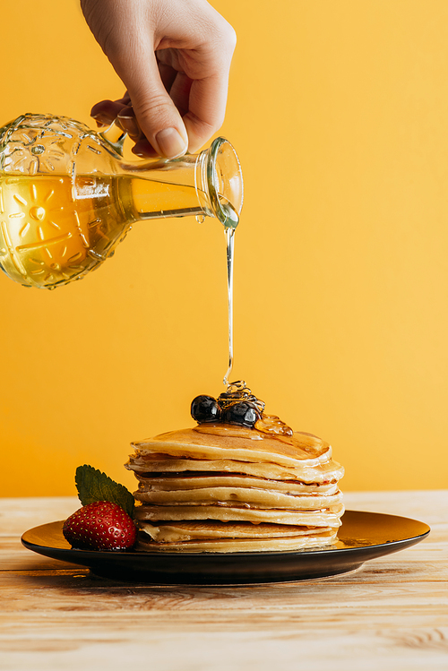 cropped shot of person pouring maple syrup onto stack of pancakes