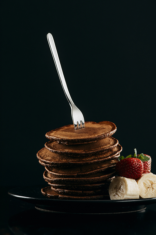 delicious stacked pancakes pierced with fork on black
