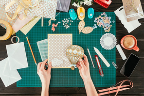 cropped image of woman adding wooden balloon to scrapbooking postcard cover