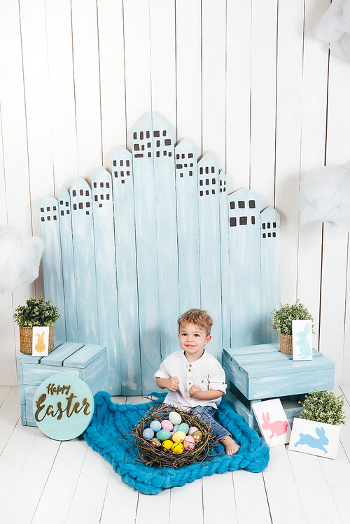 adorable little kid sitting in easter decorated room with nest of colorful eggs